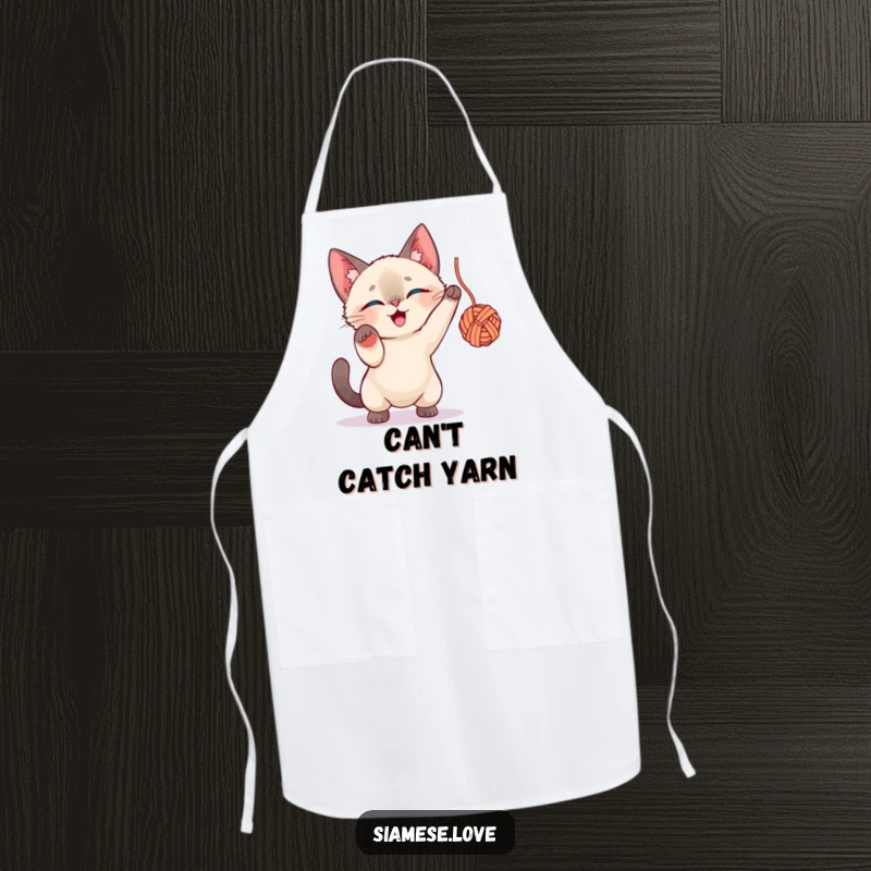 Funny Siamese Cat Apron: A Siamese cat character intensely focused on batting a ball of yarn while cooking.