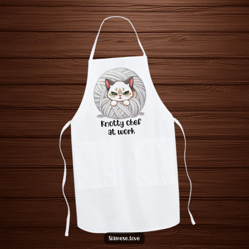 Funny cooking apron showcasing a Siamese cat with a mischievous smirk, hiding behind a ball of yarn. Practical and humorous.