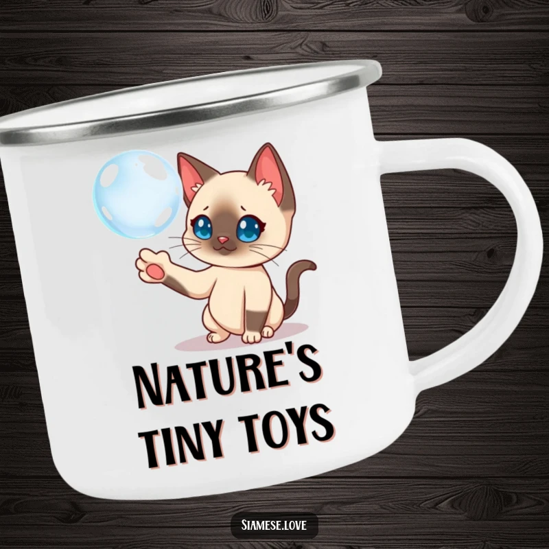 Funny Siamese cat batting a floating bubble on an enamel camping mug, ready for outdoor fun.