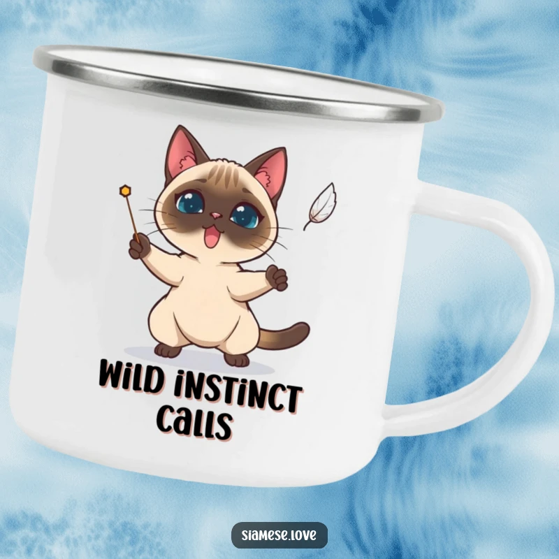 Funny Siamese cat determinedly trying to catch a falling feather on an enamel camping mug.