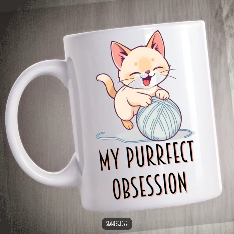 Funny mug depicting a stylized Siamese cat delightedly pouncing on a ball of yarn, capturing playful energy for a perfect gift.