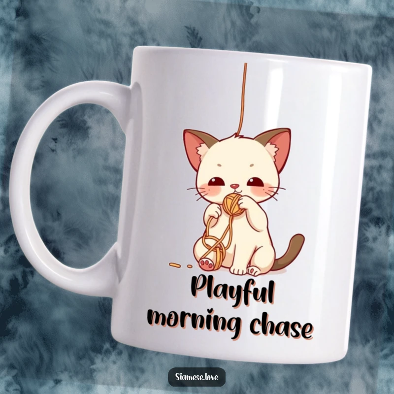 Funny kawaii Siamese cat mug, a playful kitten batting at a dangling yarn ball with an expression of focused delight.