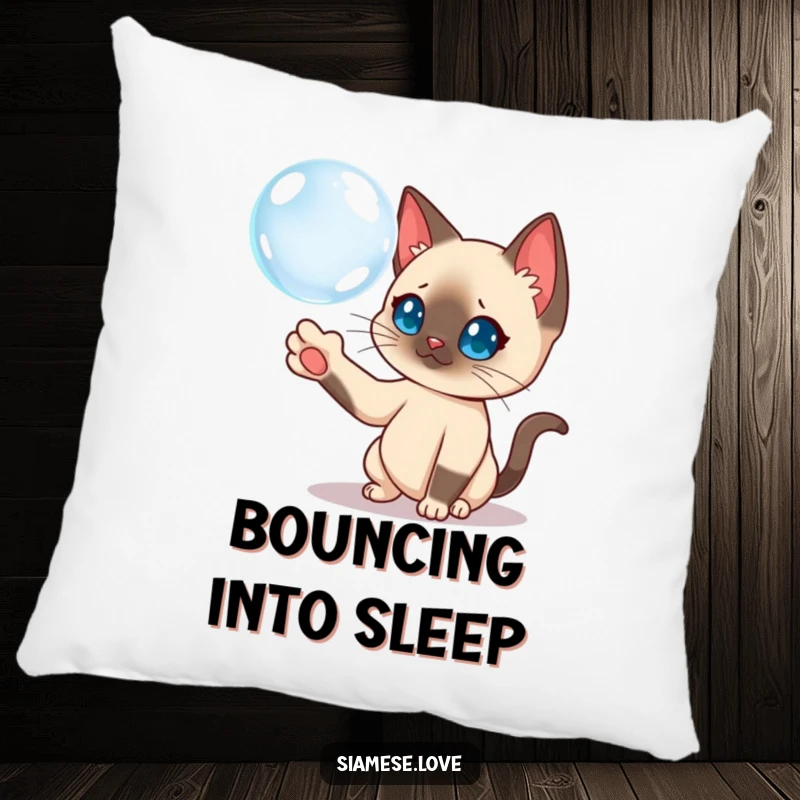 Funny Siamese cat batting a floating bubble on a decorative pillow, adding whimsical charm.