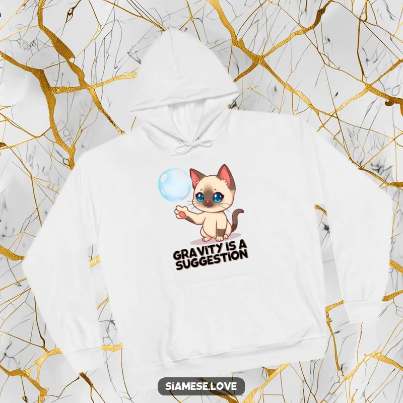 Funny Siamese cat character curiously batting a floating bubble with its paw, featured on a cozy hoodie.