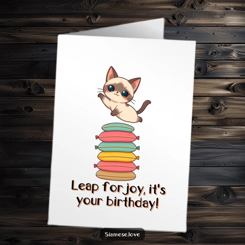 Funny Free Printable Birthday Card: Siamese cat elegantly leaping onto a tall stack of colorful cushions, celebrating.