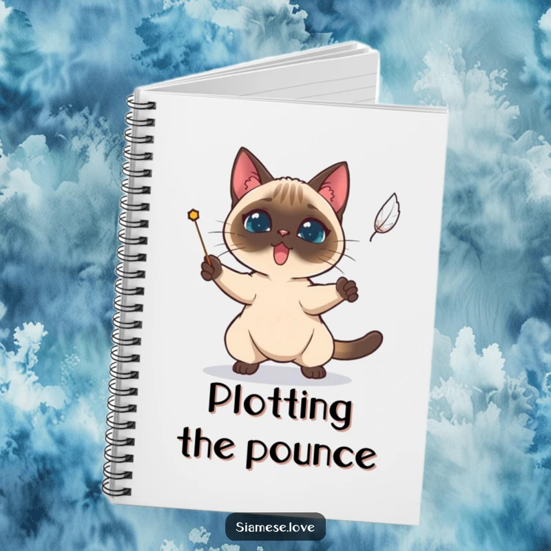 Funny Siamese cat determinedly trying to catch a falling feather on a notebook cover.