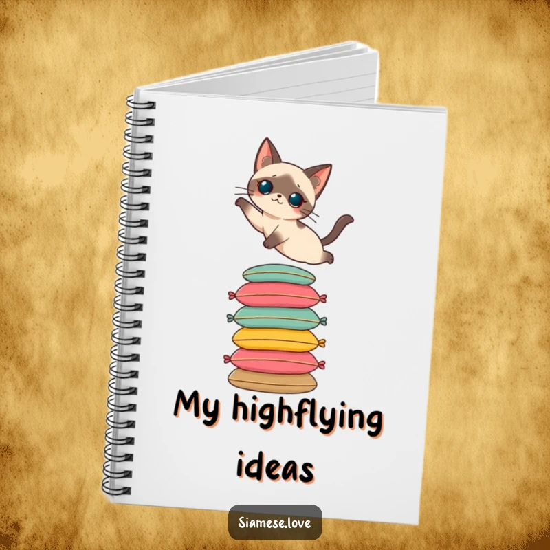 Funny notebook featuring a Siamese cat elegantly leaping onto a stack of cushions. Ideal for notes and journaling.