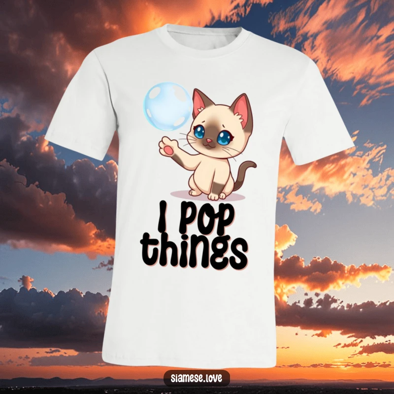 Funny Siamese cat batting a floating bubble with its paw on a t-shirt, showcasing curiosity.