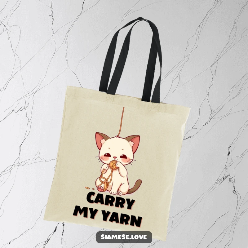 Funny tote bag with a cute kawaii Siamese cat batting playfully at a dangling yarn ball, symbolizing playful mischief.