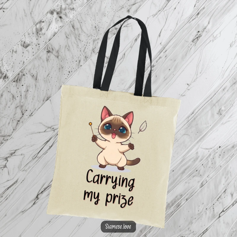 Funny Siamese cat determinedly trying to catch a falling feather on a tote bag.