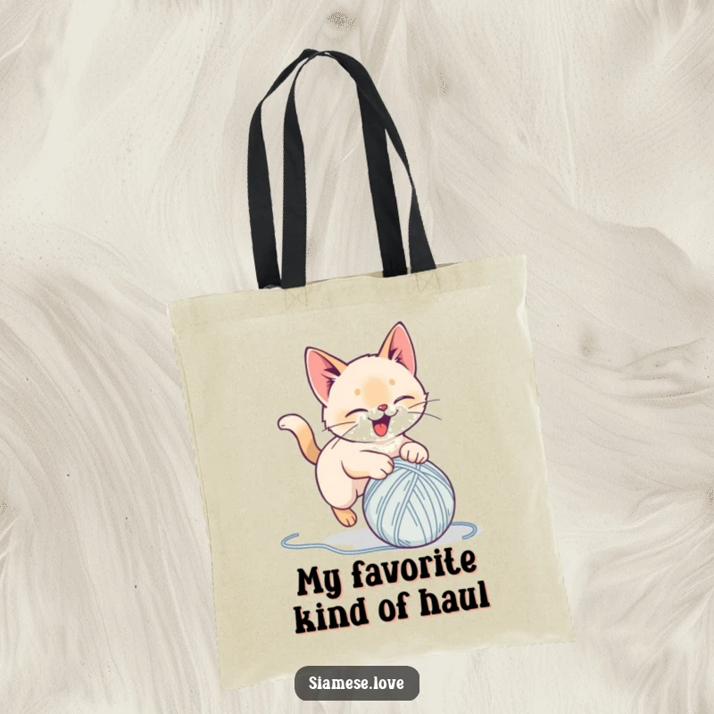 Funny tote bag featuring a stylized Siamese cat delightedly pouncing on a yarn ball, perfect for carrying items with playful feline humor.